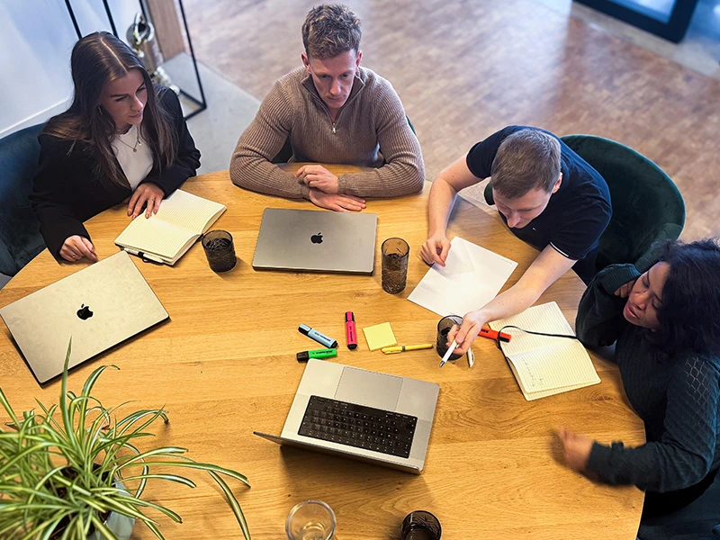 Vier mensen rond tafel met laptops in overleg over data-consultancy.