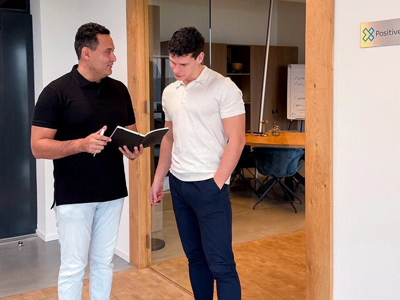 David en Max bladeren door een notitieboekje tijdens een marketing-analyse.