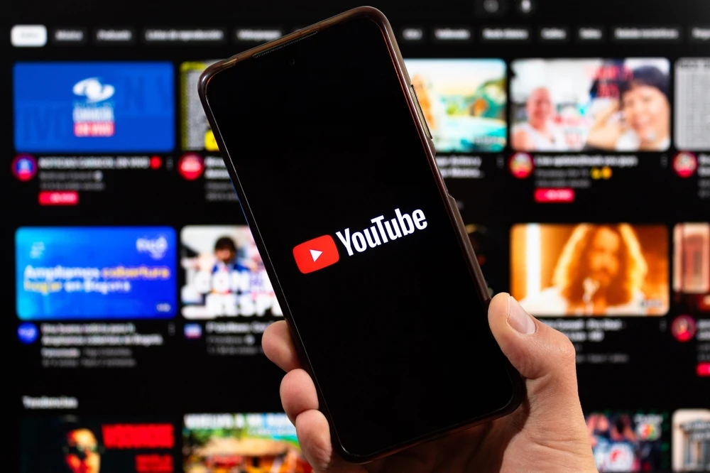 Smartphone met YouTube-logo in beeld, met video-overzicht op de achtergrond.