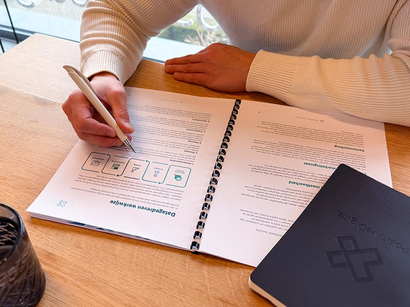 Persoon maakt aantekeningen in een planner aan een bureau.