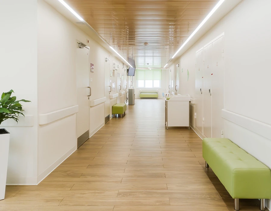 Moderne, lichte zorggang met groene zitbanken en houten vloer.