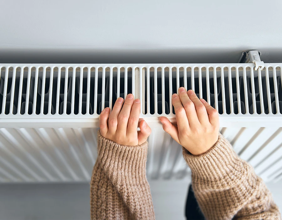 Handen bij een witte radiator voor een warme woning.
