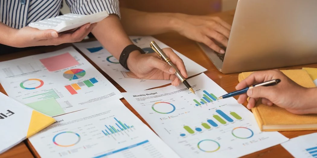 Team analyseert grafieken en budgetrapporten met laptop, rekenmachine en notities.