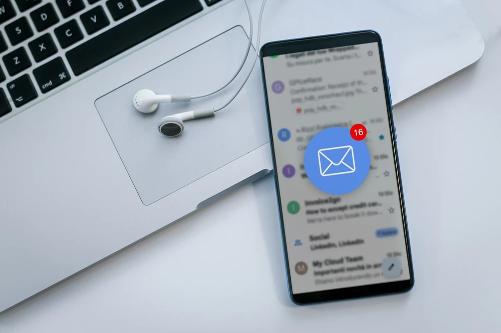 Smartphone met nieuwe e-mailmelding naast laptop op bureau.