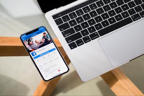 Facebook on mobile phone next to a MacBook